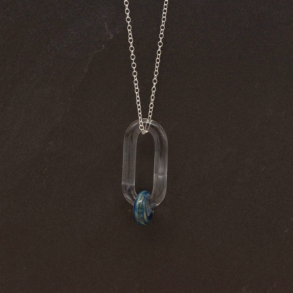 clear glass link which passes through a bead made from blue and green glass, hanging from a sterling silver chain, dark background.