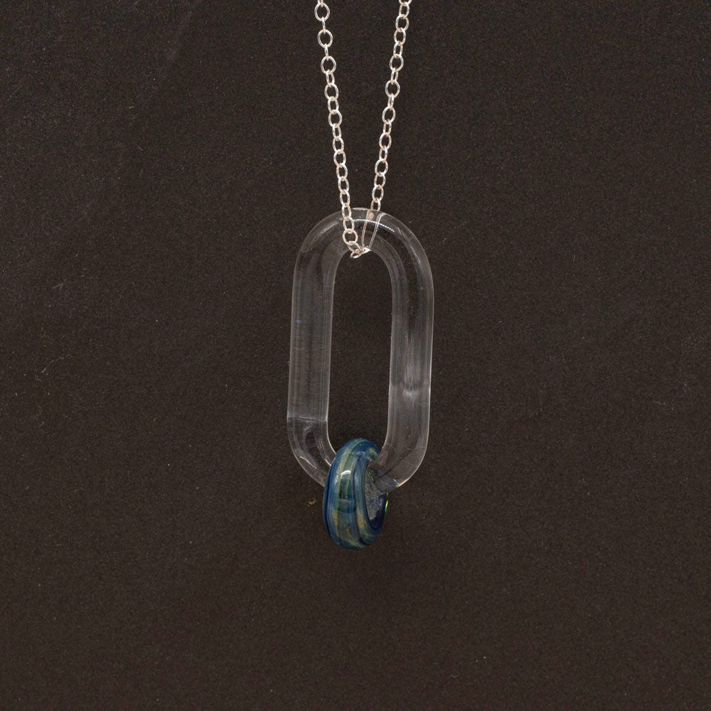 Close up of a clear glass link which passes through a bead made from blue and green glass, hanging from a sterling silver chain, dark background.