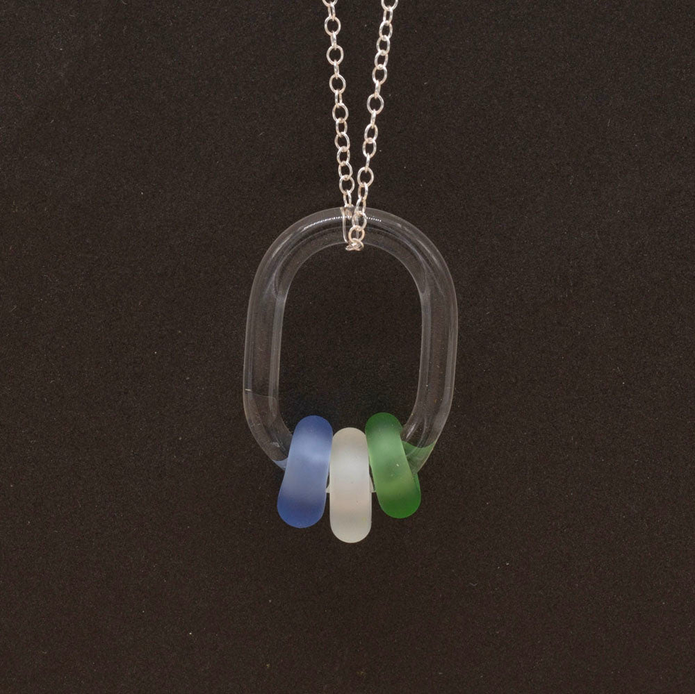 Close up of clear glass link passing through blue, clear and green on a sterling silver chain, dark background.