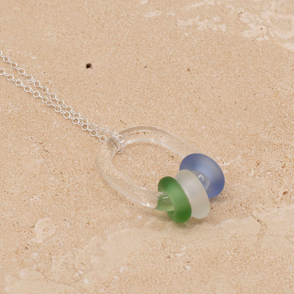 Necklace with clear glass link passing through green, clear and blue beads on sterling silver chain, sandstone tile.