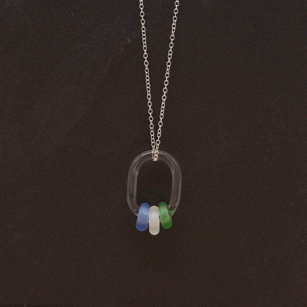 Clear glass link passing through blue, clear and green on a sterling silver chain, dark background.
