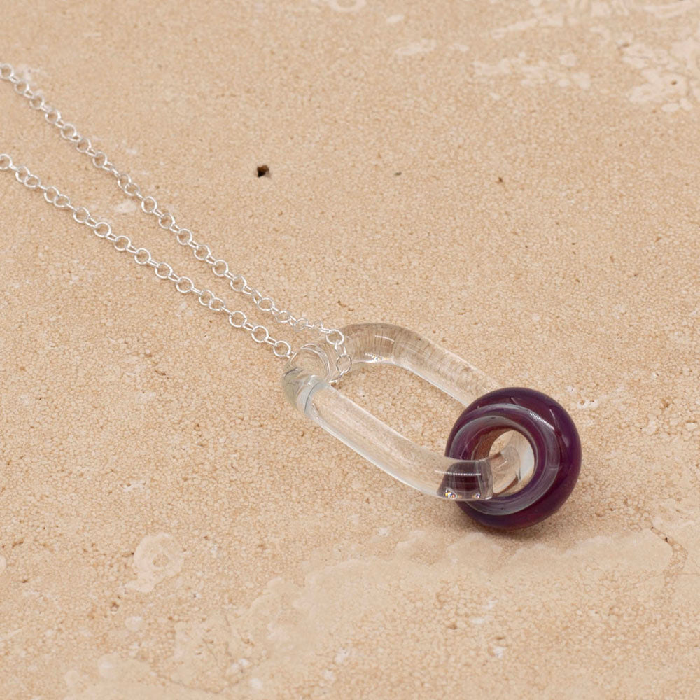 Clear glass link with purple iris bead and sterling silver chain photographed on a sandstone tile