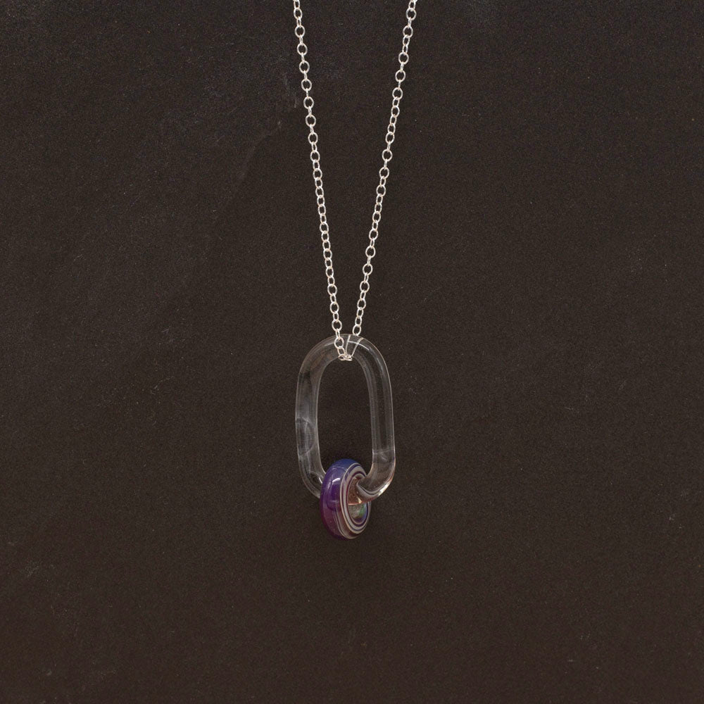 Clear glass link with purple iris bead. The bead is purple and has silver coloured spirals at the side. Hanging on a sterling silver chain. Dark background.