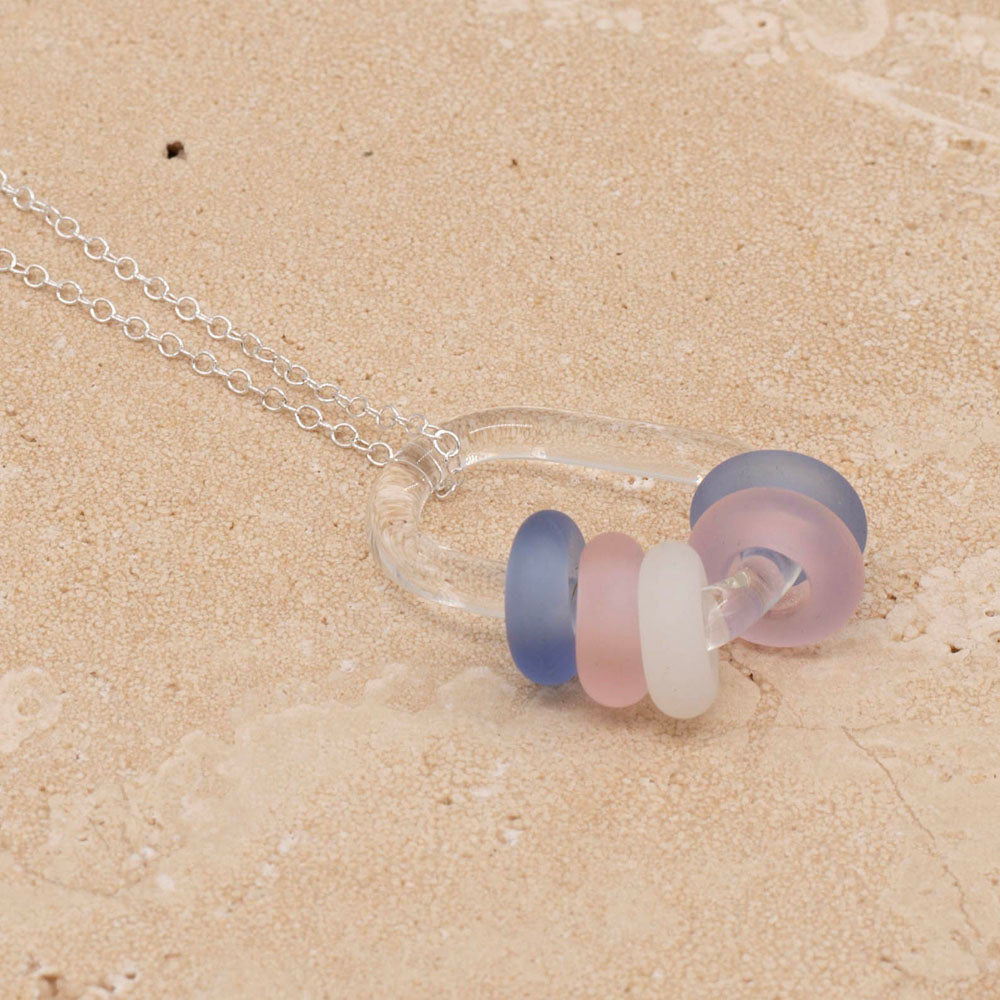 Necklace with clear glass link and pale blue, pink and white beads on a sterling chain photographed on a sandstone tile.