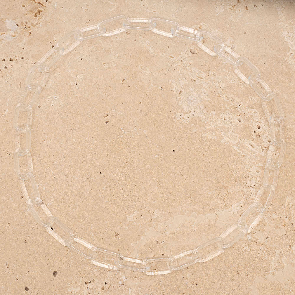 Clear glass chain link necklace photographed from above on sandstone tile.