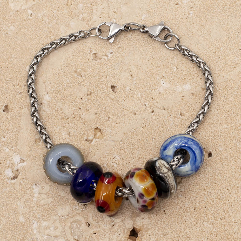 Six glass beads on a stainless steel bracelet. The beads are pale blue with silver dots, dark blue with a large cream dot, yellow with raised red and black dots, pale grey with multicolour splodges,  black with silver and ivory and  creamy blue swirls. The bracelet fastens with  double lobster clasp.