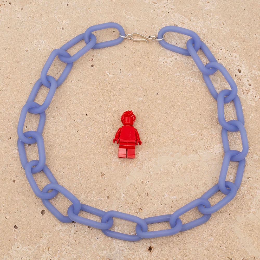 A necklace made from pale blue frosted glass links and fastened with a silver hook and eye. Photographed from above with a Lego figure for scale.