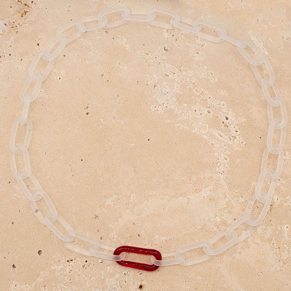 Clear frosted glass chain necklace with a single red link, photographed from above.