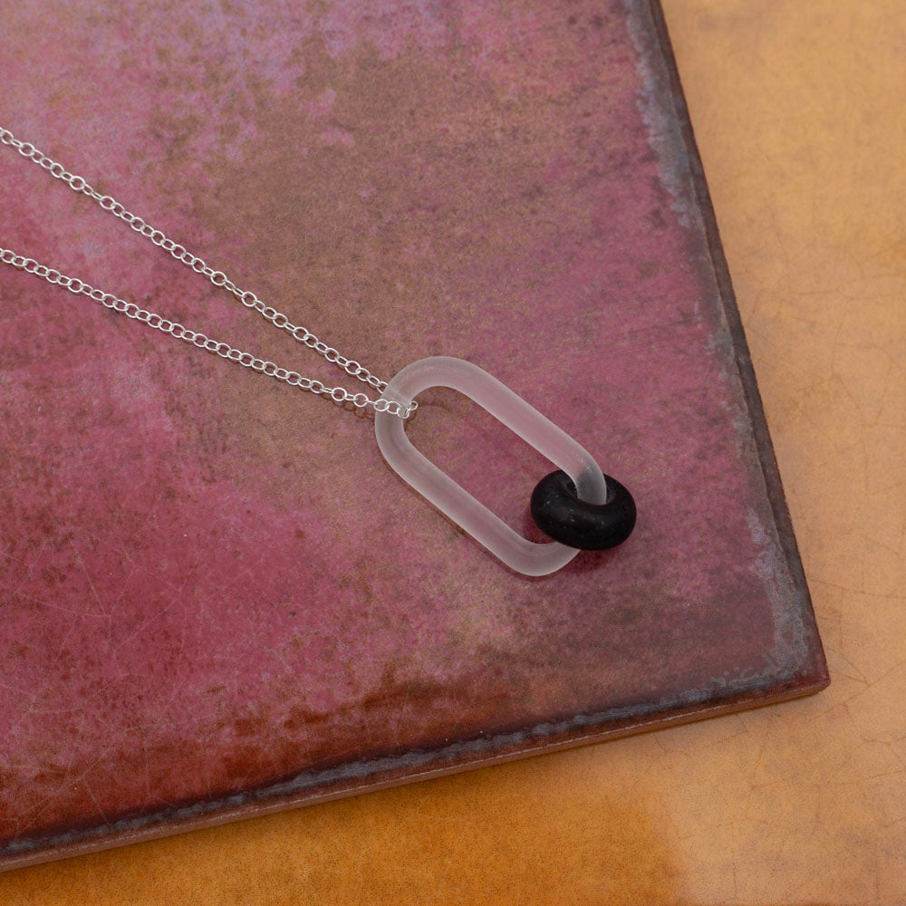 Necklace with clear link and dark brown bead made from a recycled beer bottle, photographed on pink and yellow tiles