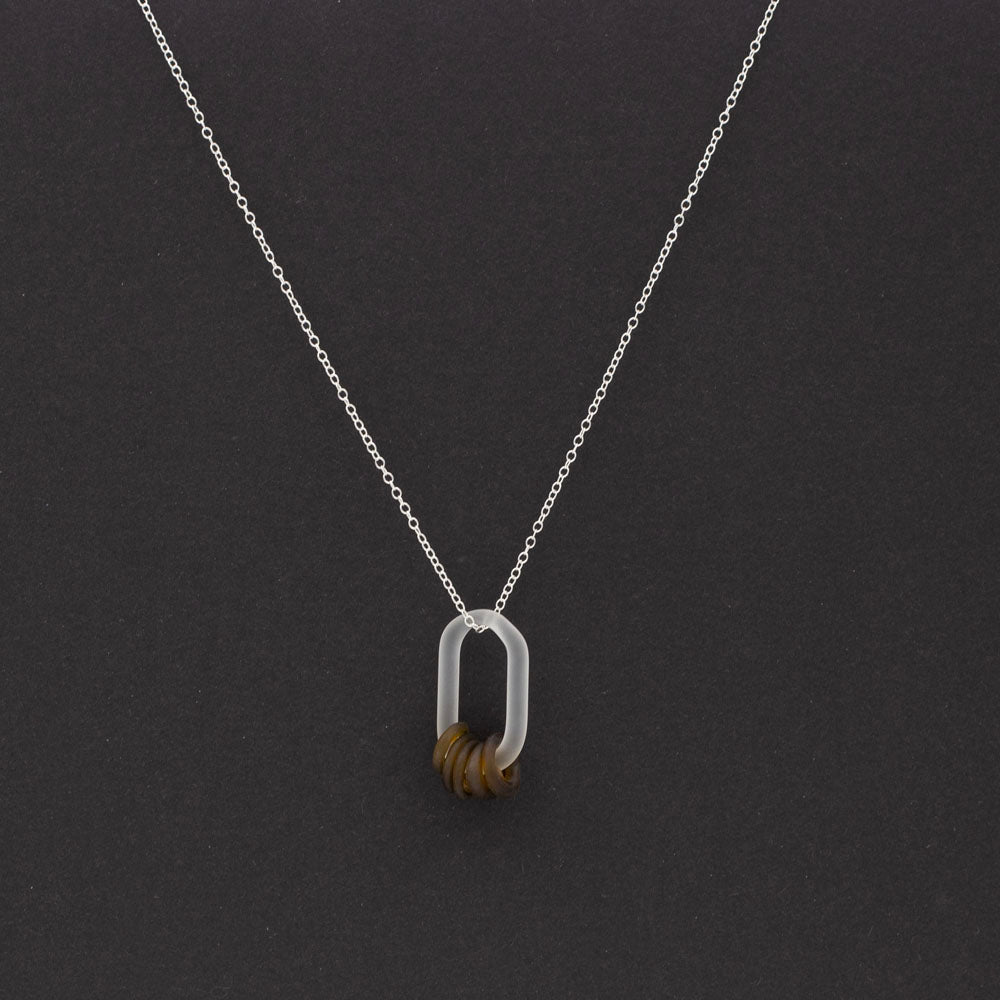 Dark background, a frosted link made from clear glass which passes through five beads. The beads are made from a marmite bottle so are brown. They also have a frosted finish. The link hangs from a sterling silver chain.