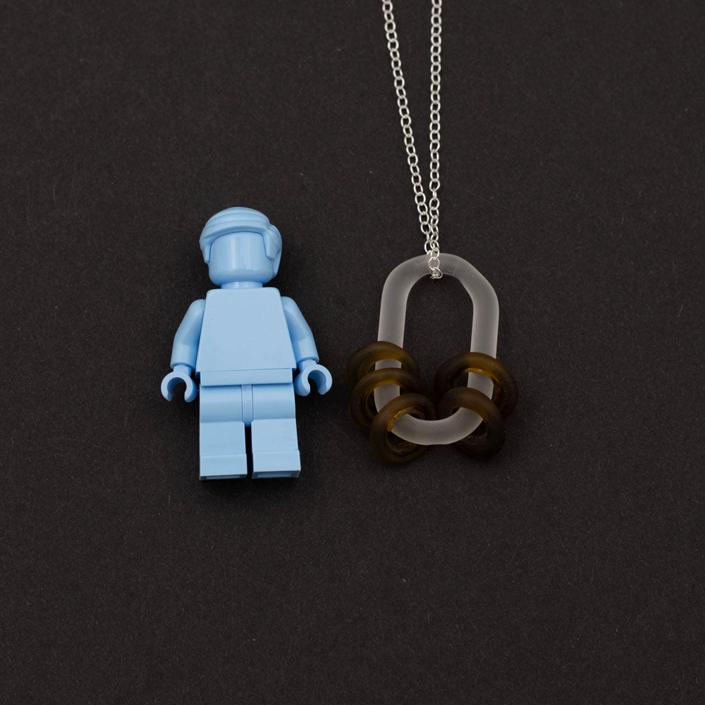 Lego figure with Close up of a frosted link made from clear glass which passes through five beads. The beads are made from a marmite bottle so are brown. 
