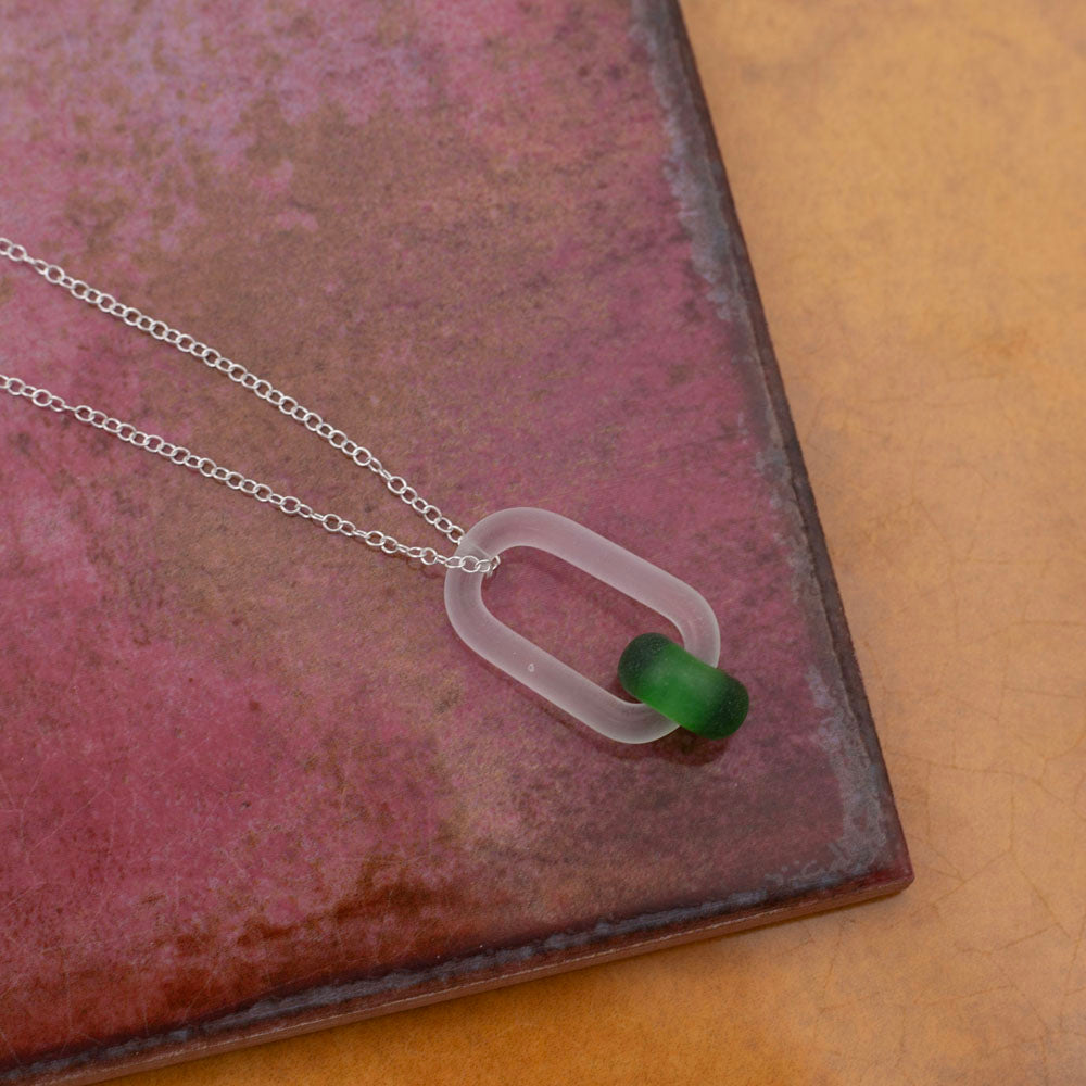 Frosted clear glass link and green gin bottle glass bead necklace. Photographed on pink and yellow tiles.