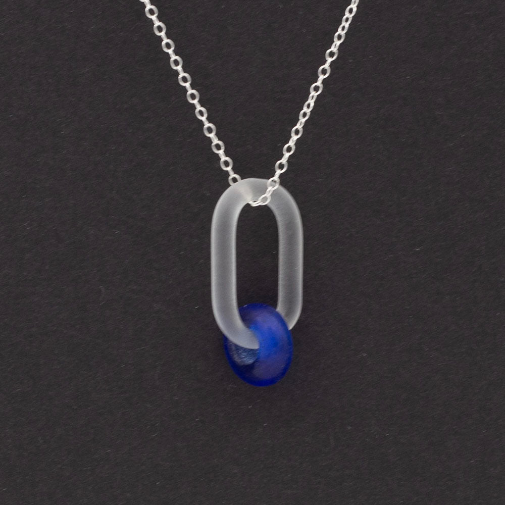 Close up on dark background. Frosted clear glass link necklace. The link passes through a bead made form recycled blue sherry bottle glass, and the bead has a frosted finish. The link hangs from a sterling silver chain.