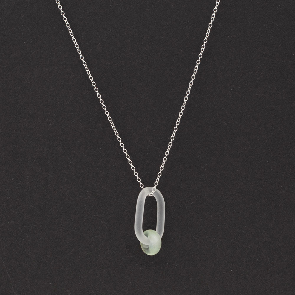 clear link which passes through a bead made from a recycled pale green wine bottle. Link and beads have a frosted finish. The link hangs from a sterling silver chain.