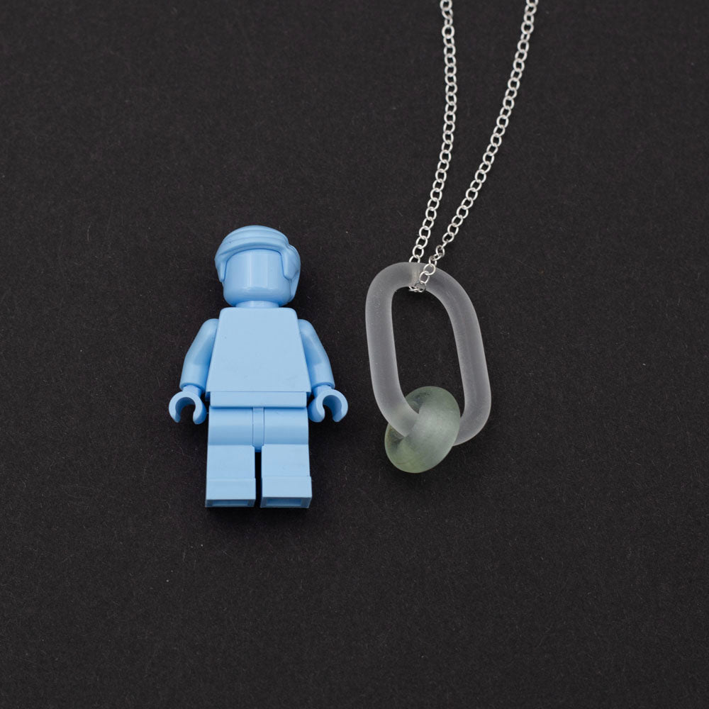 Lego figure with clear link which passes through a bead made from a recycled pale green wine bottle. Link and beads have a frosted finish. The link hangs from a sterling silver chain.