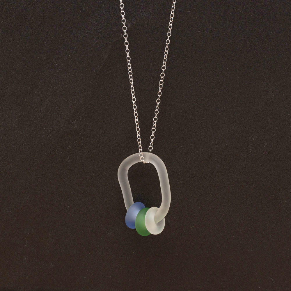 Clear link which passes through beads in blue, green and clear glass. Link and beads have a frosted finish. The link hangs from a sterling silver chain. Dark background.