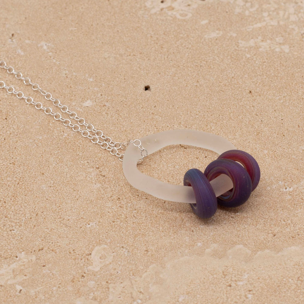 Sandstone tile with clear link which passes through beads in blueberry purple glass. Link and beads have a frosted finish. The link hangs from a sterling silver chain.  