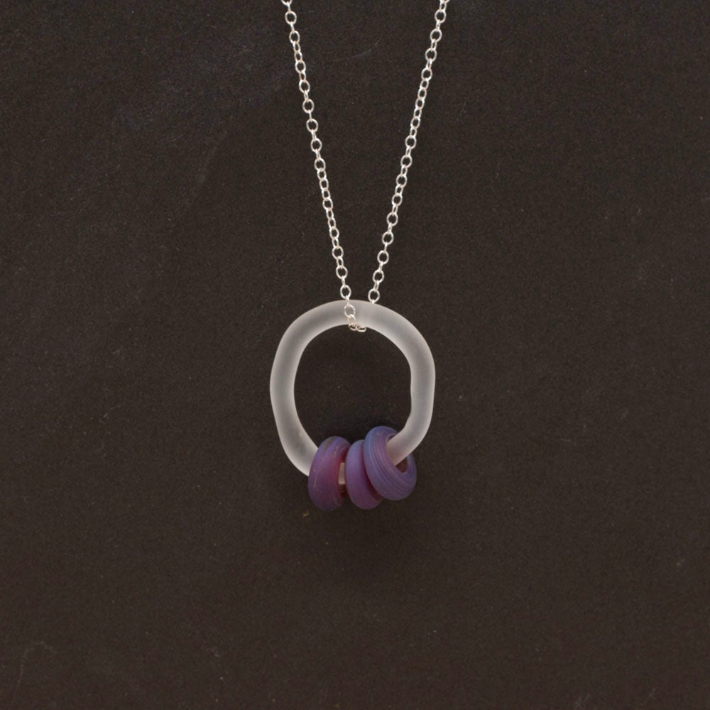 Clear link which passes through beads in blueberry purple glass. Link and beads have a frosted finish. The link hangs from a sterling silver chain. Shown on a dark background.