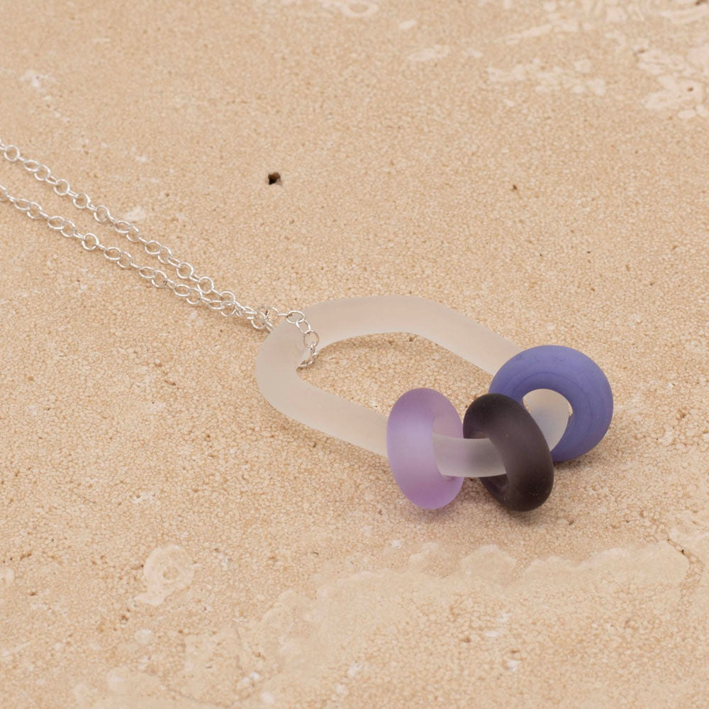 Necklace made with a frosted clear glass link which passes through three beads. The beads are made from pink, lilac and plum glass and all three have a frosted finish. The necklace is finished with a sterling silver chain.