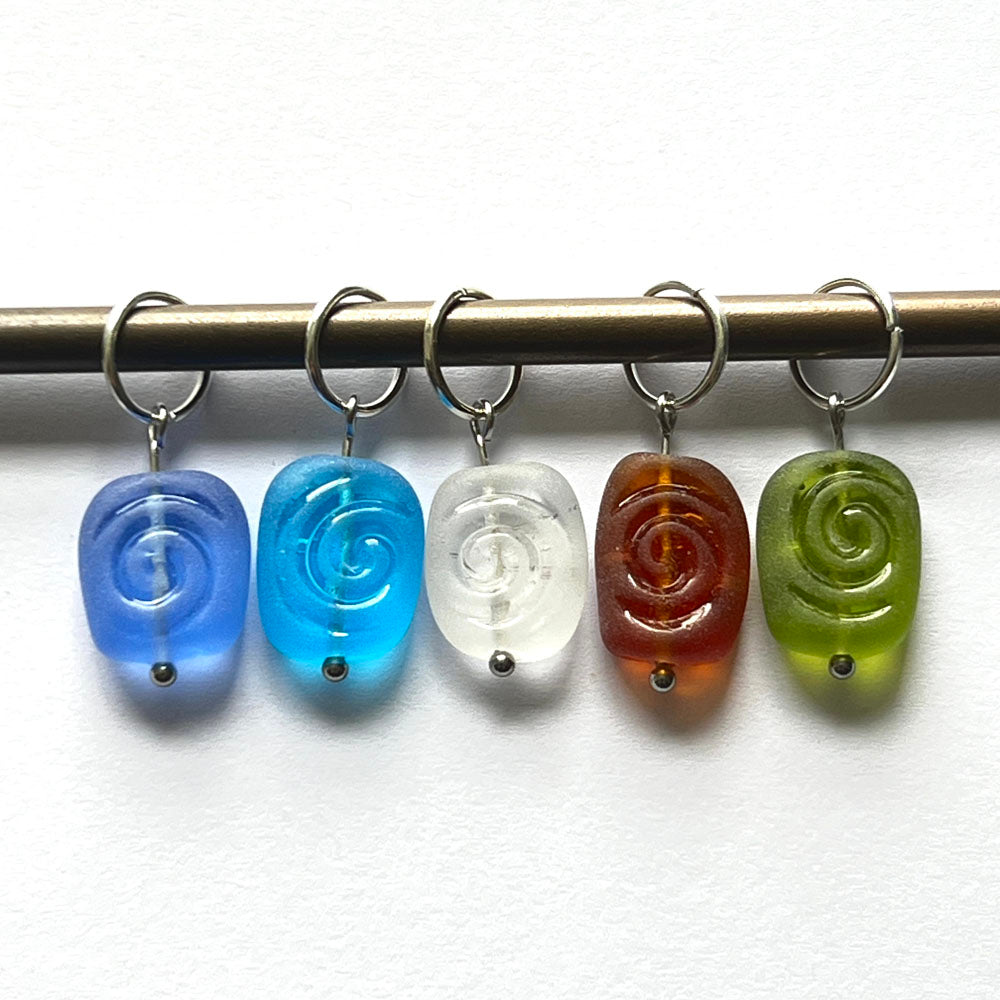 Frosted beads with spiral imprint in blue, turquoise, clear, amber and green glass. The beads hang from jump rings to make stitch markers.