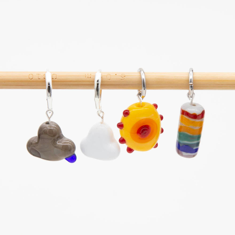 Four stitch markers with weather themed beads. Grey cloud with raindrop, white cloud, teloow sun and tube bead with rainbow stripes. The beads hang from jump wings and latch back hooks.