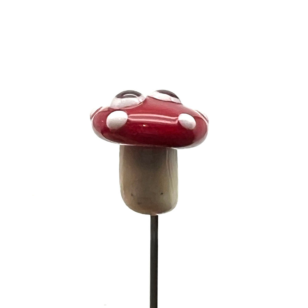 side view of glass mushroom showing metal pin, cream glass stalk, red cap with white dots and two cartoon style eyes