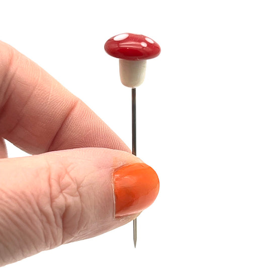 Pin with mushroom top. The mushroom has a cream stalk and a rounded red cap with white spots.