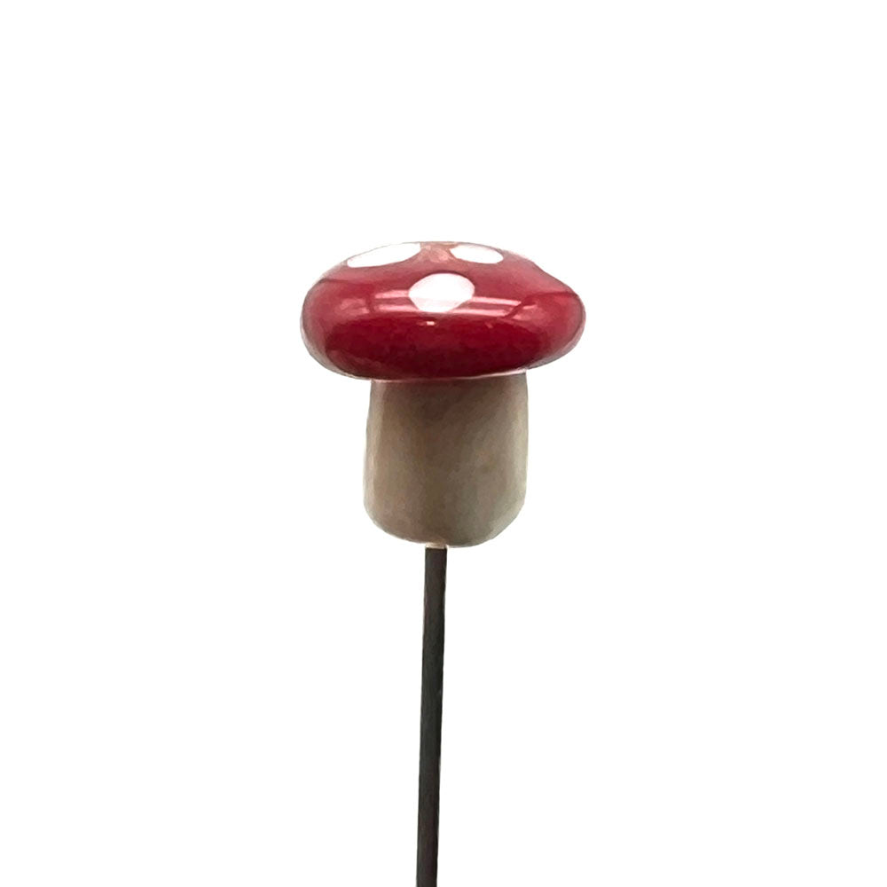 side view of glass mushroom pin showing cream stalk, and rounded red cap with white dots.