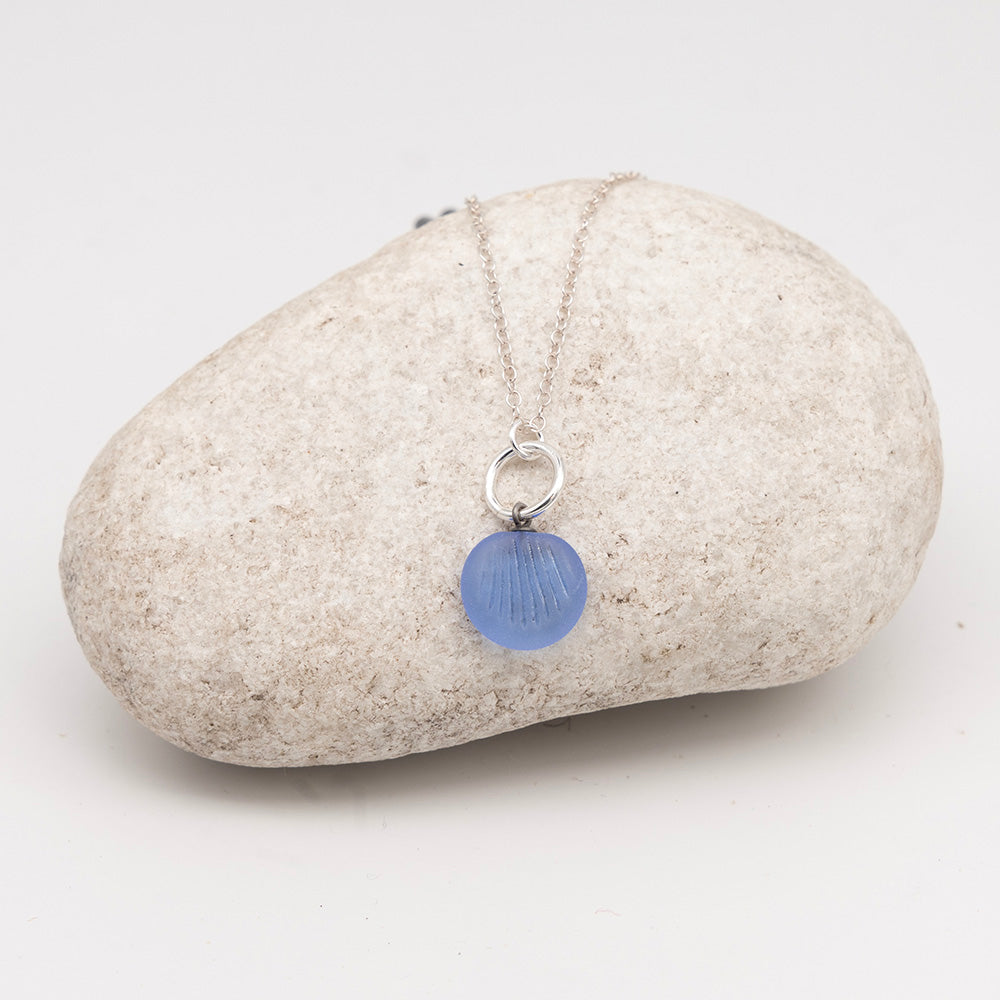 frosted blue glass shell charm necklace on a pale grey rock