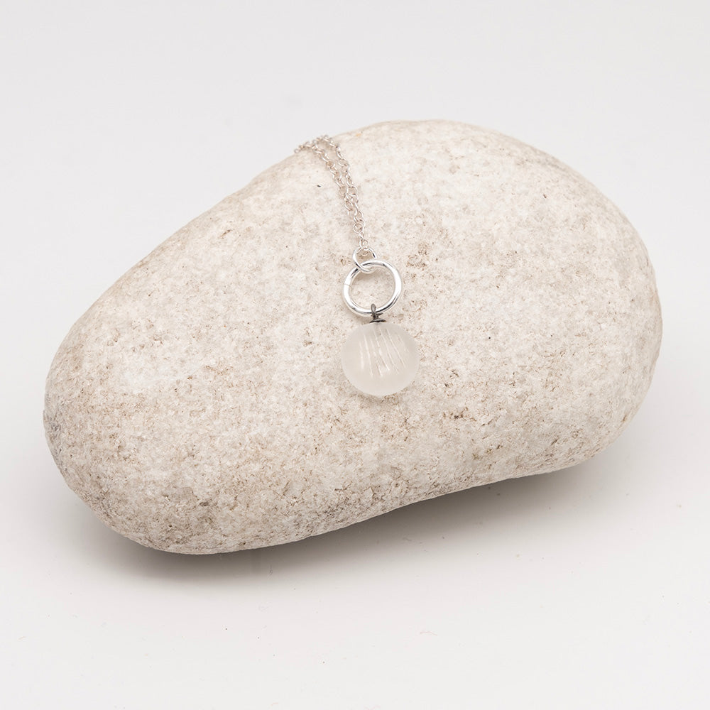 frosted clear glass shell charm necklace on a pale grey rock