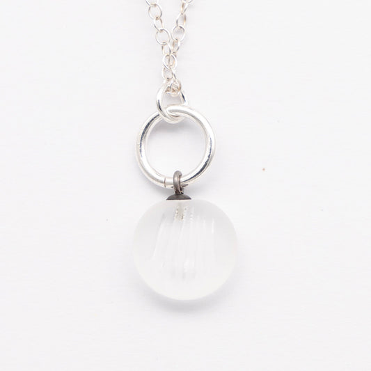 Close up of clear frosted glass charm with shell imprint on a plain white background. The charm is frosted, and spiral is shiny. The charm hangs on a large silver jump ring. The necklace is completed with a small silver jump ring and silver chain.