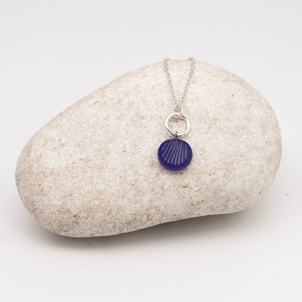 frosted dark blue glass shell charm necklace on a pale grey rock