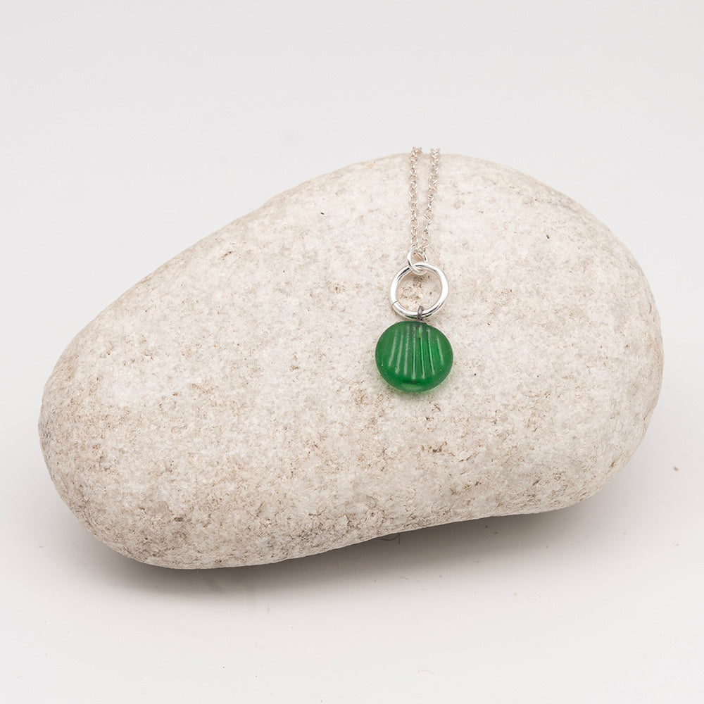 frosted green glass shell charm necklace on a pale grey rock