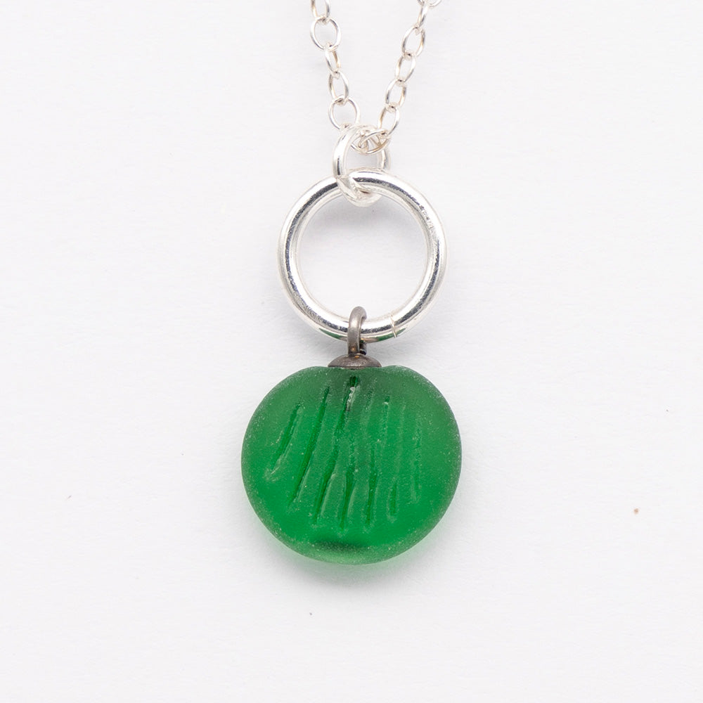 Close up of green frosted glass charm with shell imprint on a plain white background. The charm is frosted, and spiral is shiny. The charm hangs on a large silver jump ring. The necklace is completed with a small silver jump ring and silver chain.