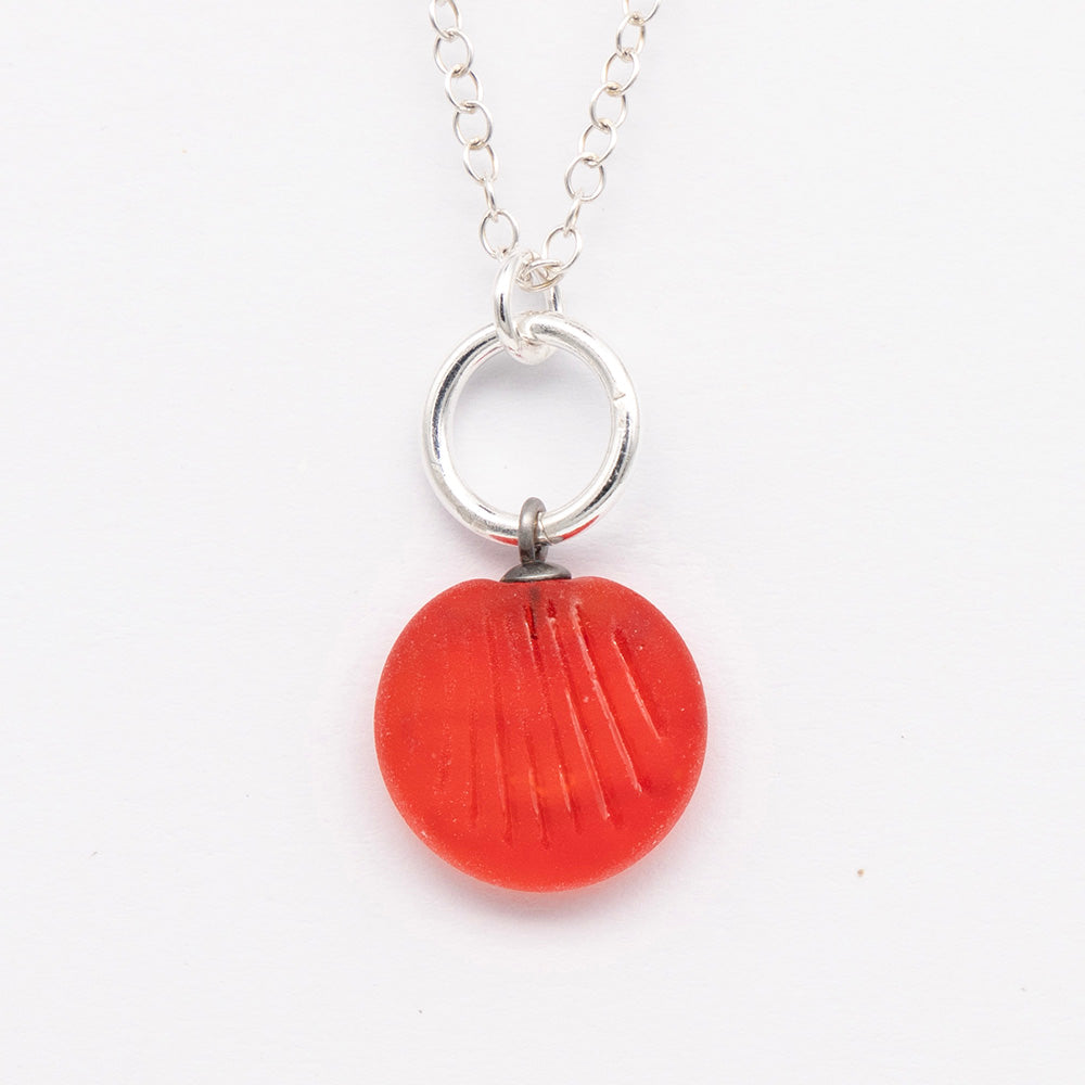 Close up of orange frosted glass charm with shell imprint on a plain white background. The charm is frosted, and spiral is shiny. The charm hangs on a large silver jump ring. The necklace is completed with a small silver jump ring and silver chain.