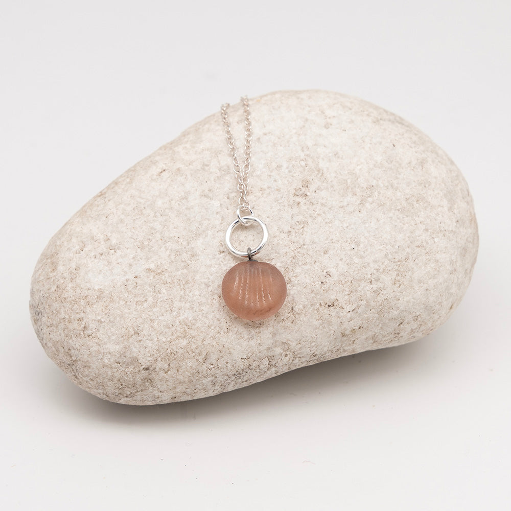 frosted pink glass shell charm necklace on a pale grey rock