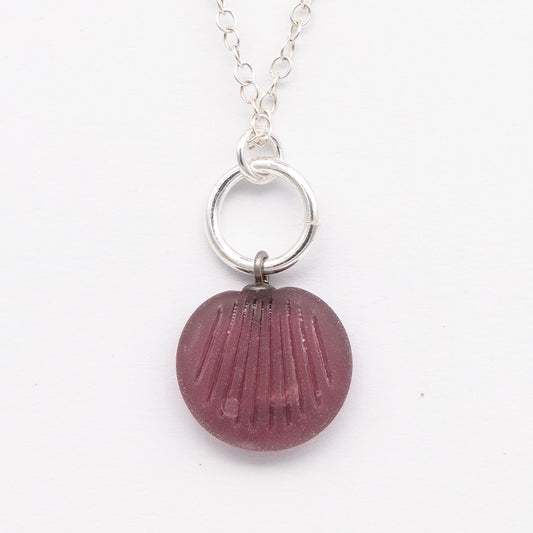 Close up of purple frosted glass charm with shell imprint on a plain white background. The charm is frosted, and spiral is shiny. The charm hangs on a large silver jump ring. The necklace is completed with a small silver jump ring and silver chain.