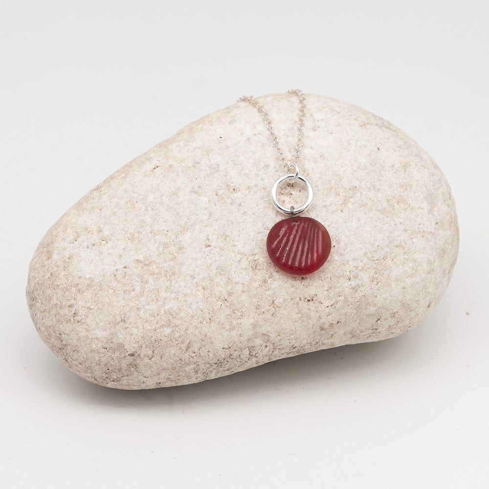 frosted red glass glass shell charm necklace on a pale grey rock