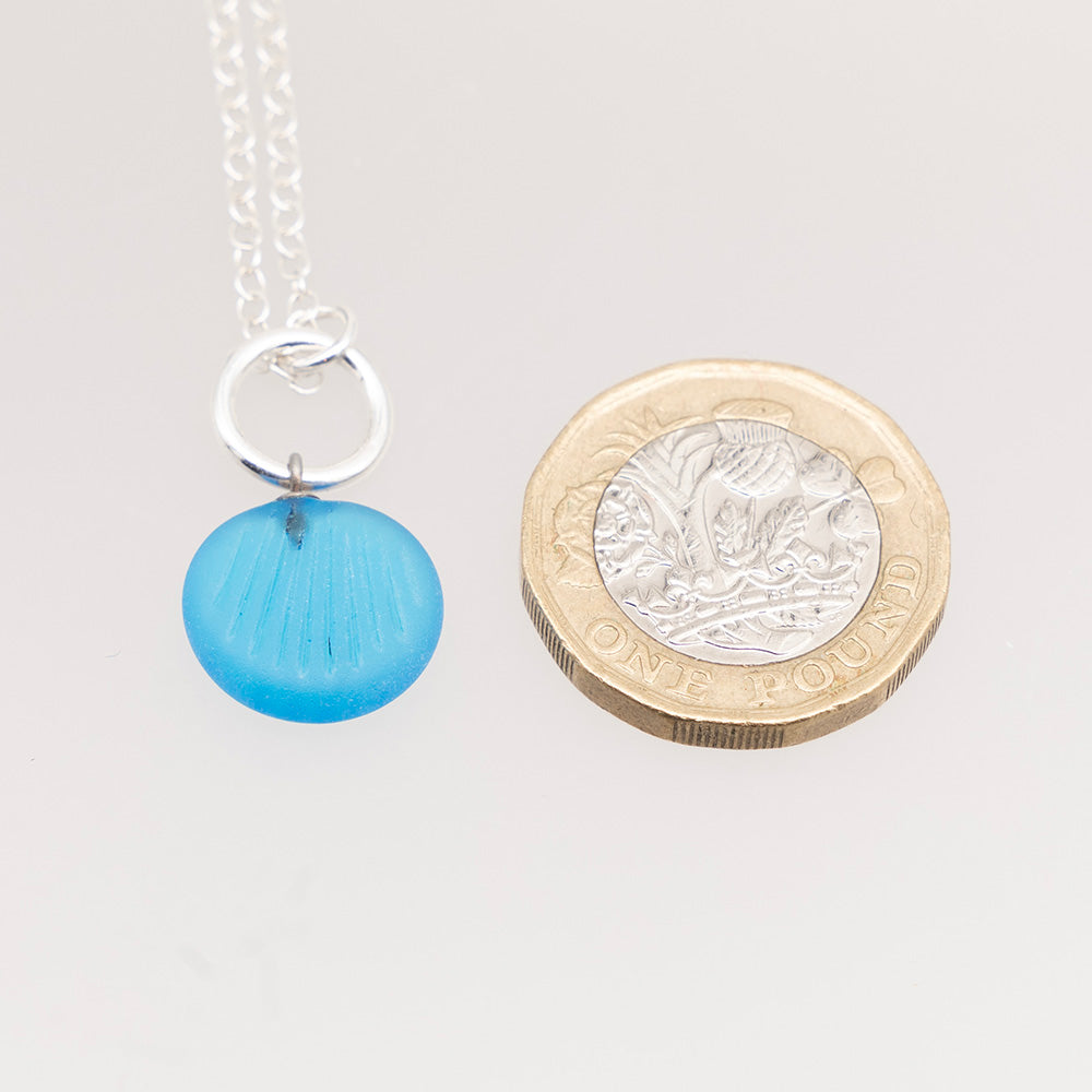 Shell imprint necklace shown with pound coin for scale. The glass charm is roughly half the height of the coin.