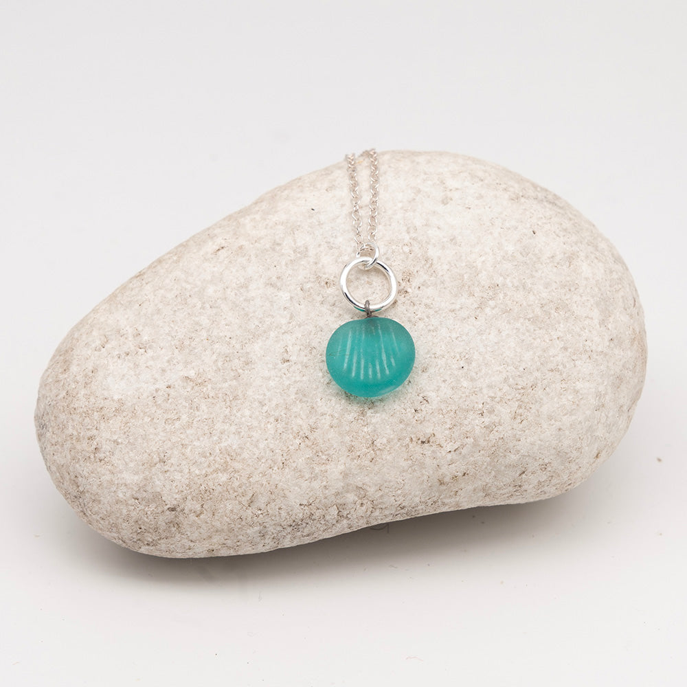 frosted teal glass shell charm necklace on a pale grey rock