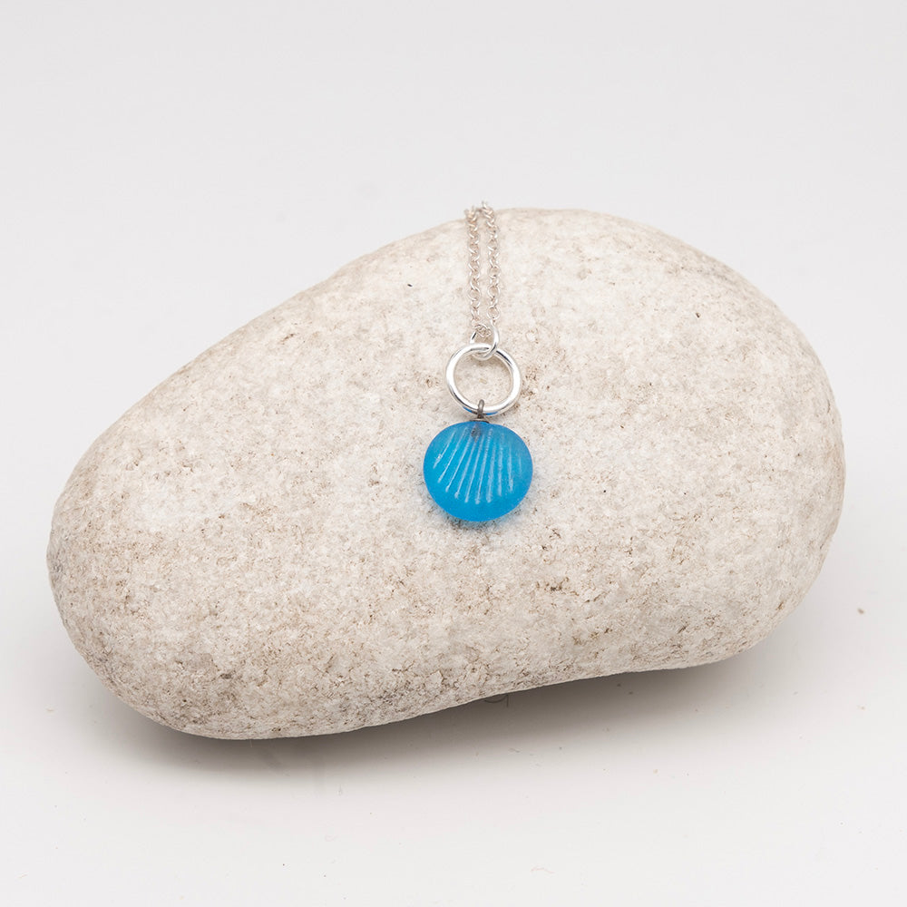 frosted turquoise glass shell charm necklace on a pale grey rock