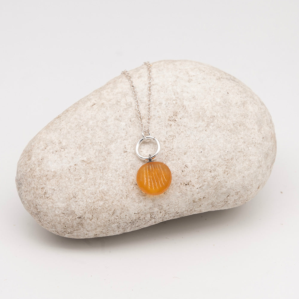 frosted yellow glass shell charm necklace on a pale grey rock