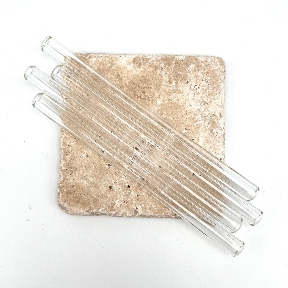 Four clear glass straws sit across a small sandstone tile. Photo taken from above.