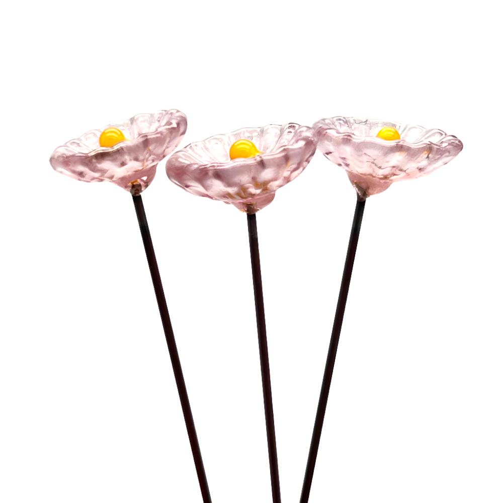 three speckled pink glass daisies with yellow centres on metal stakes