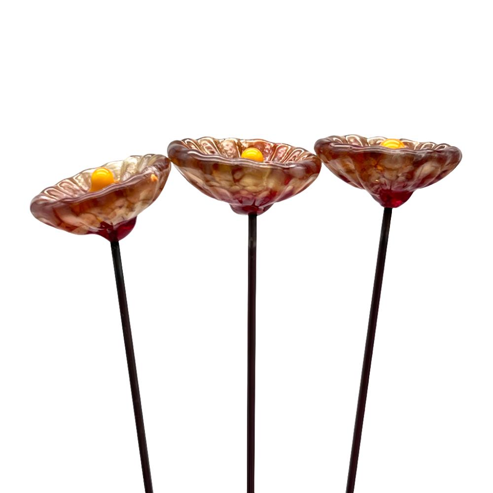 three speckled red glass daisies with yellow centres on metal stakes