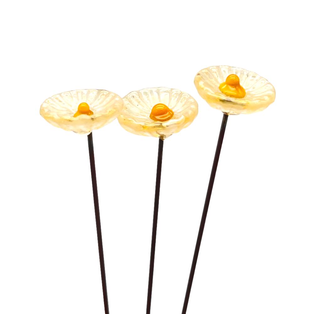 three speckled yellow glass daisies with yellow centres on metal stakes