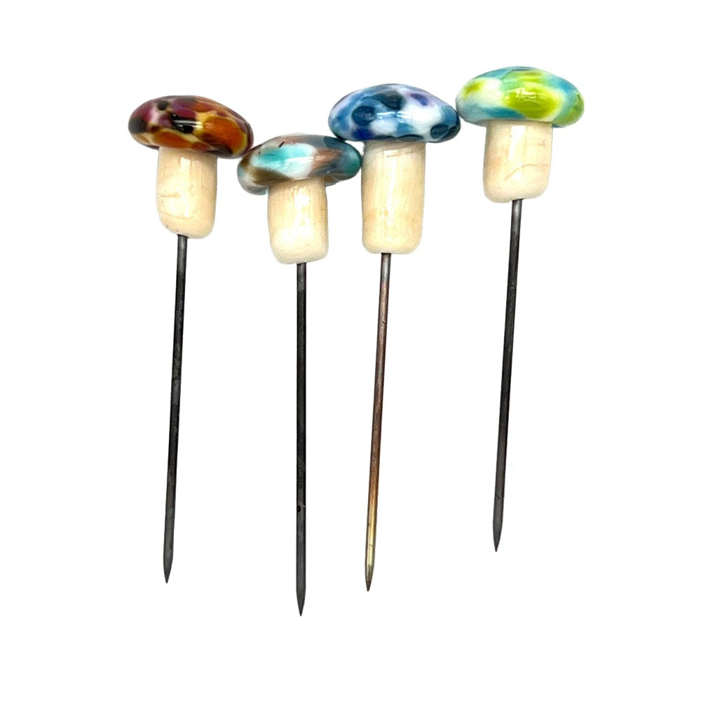 Set of four speckled mushroom pins: Four handmade glass mushroom pins with speckled caps in various colors (berry, turquoise, blue, and green), arranged in a row for display.