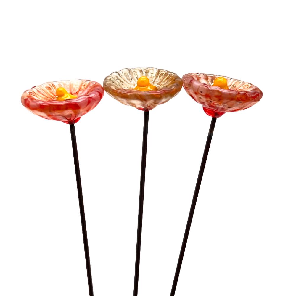 three speckled orange glass daisies with yellow centres on metal stakes