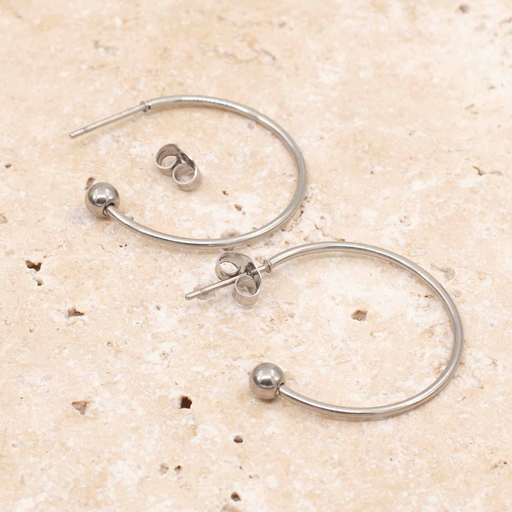 Close up of stainless steel three quarter hoop earrings with ball at end and butterfly fastening