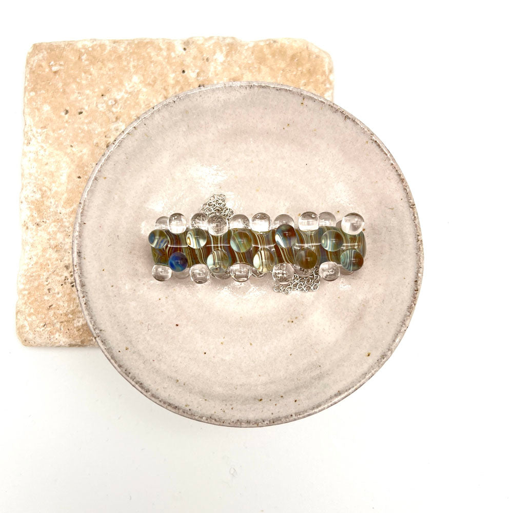 Strata glass bead necklace sitting in a small white ceramic bowl. Photographed from above.